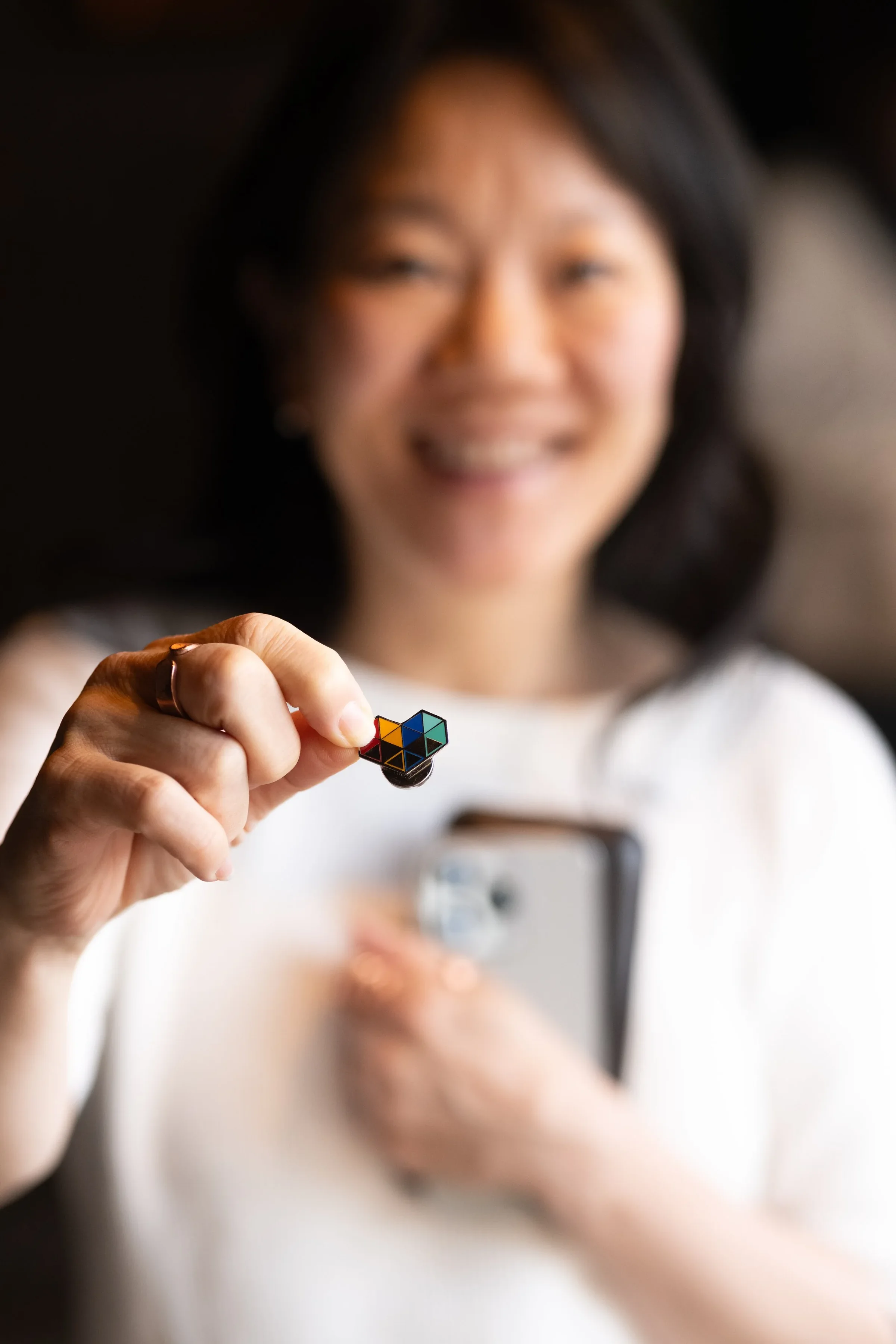 An event guest holds a small multicolored pin toward the camera.