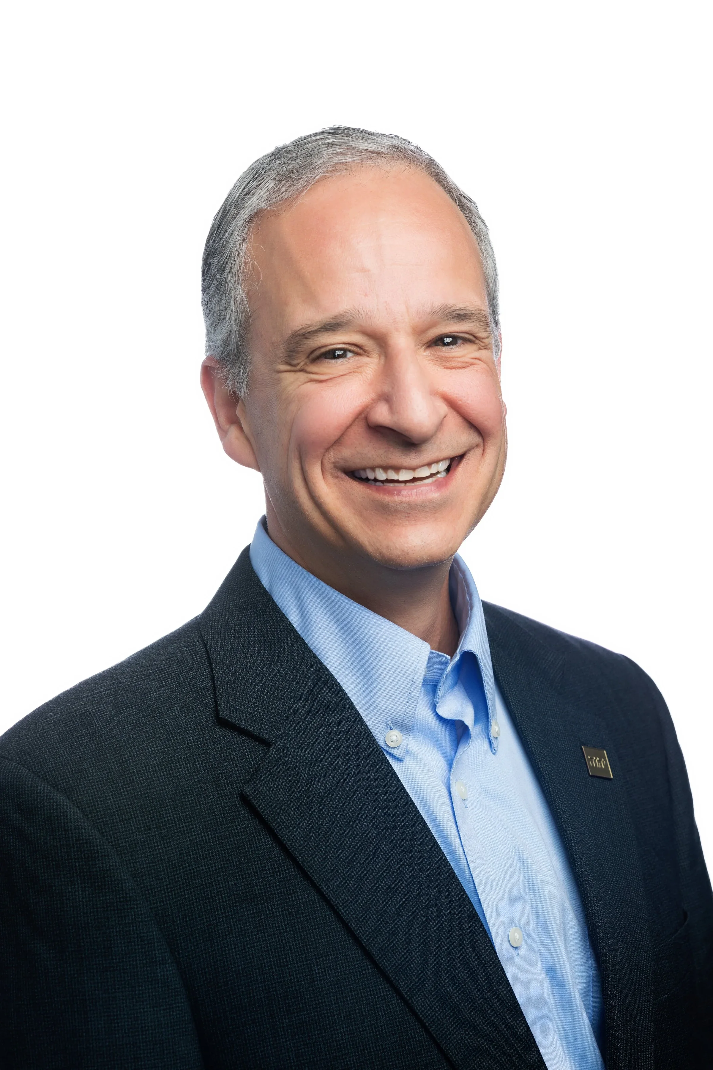 Studio headshot of a smiling man in a dark blazer and blue shirt.