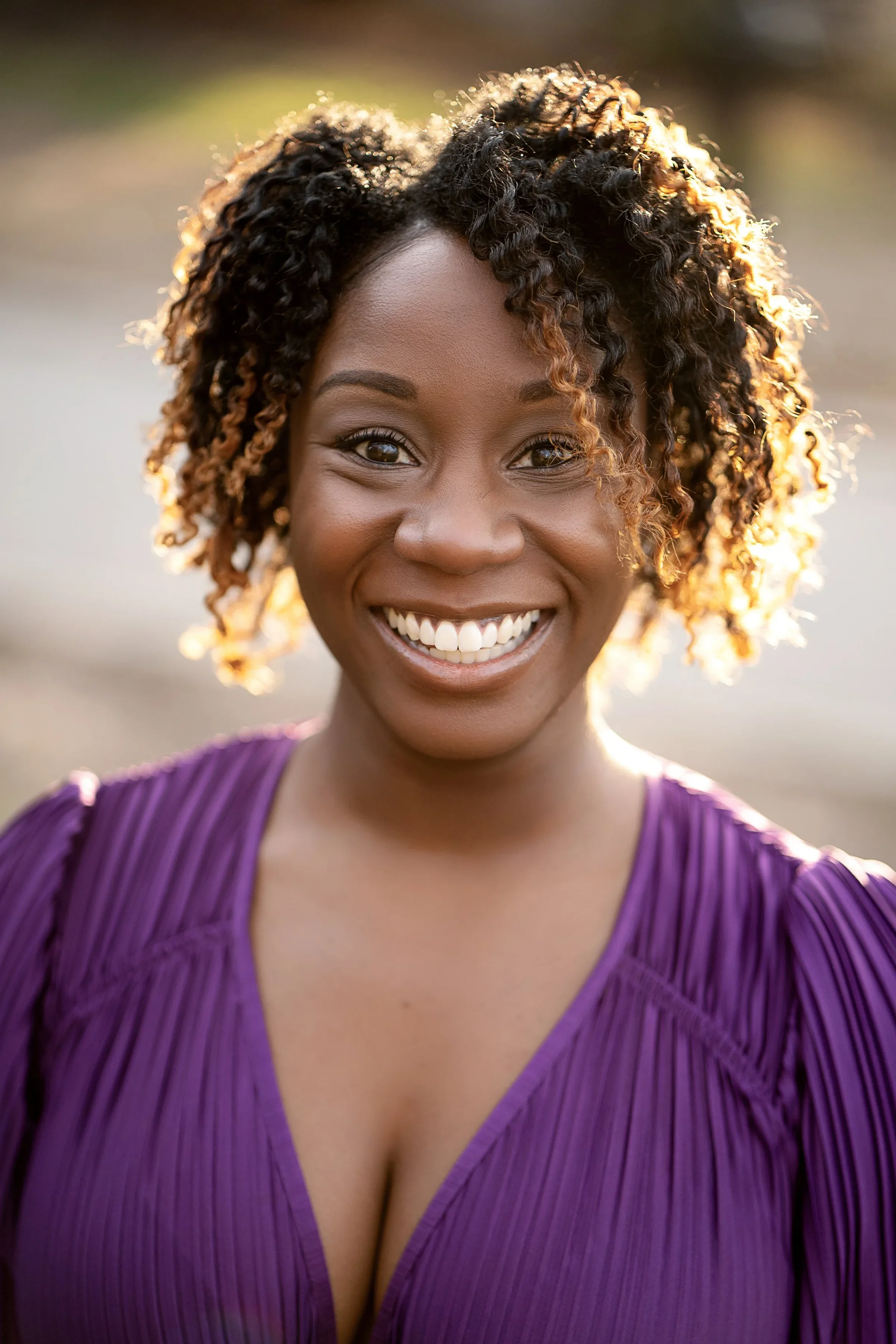 Outdoor headshot of a smiling woman in a purple blouse.