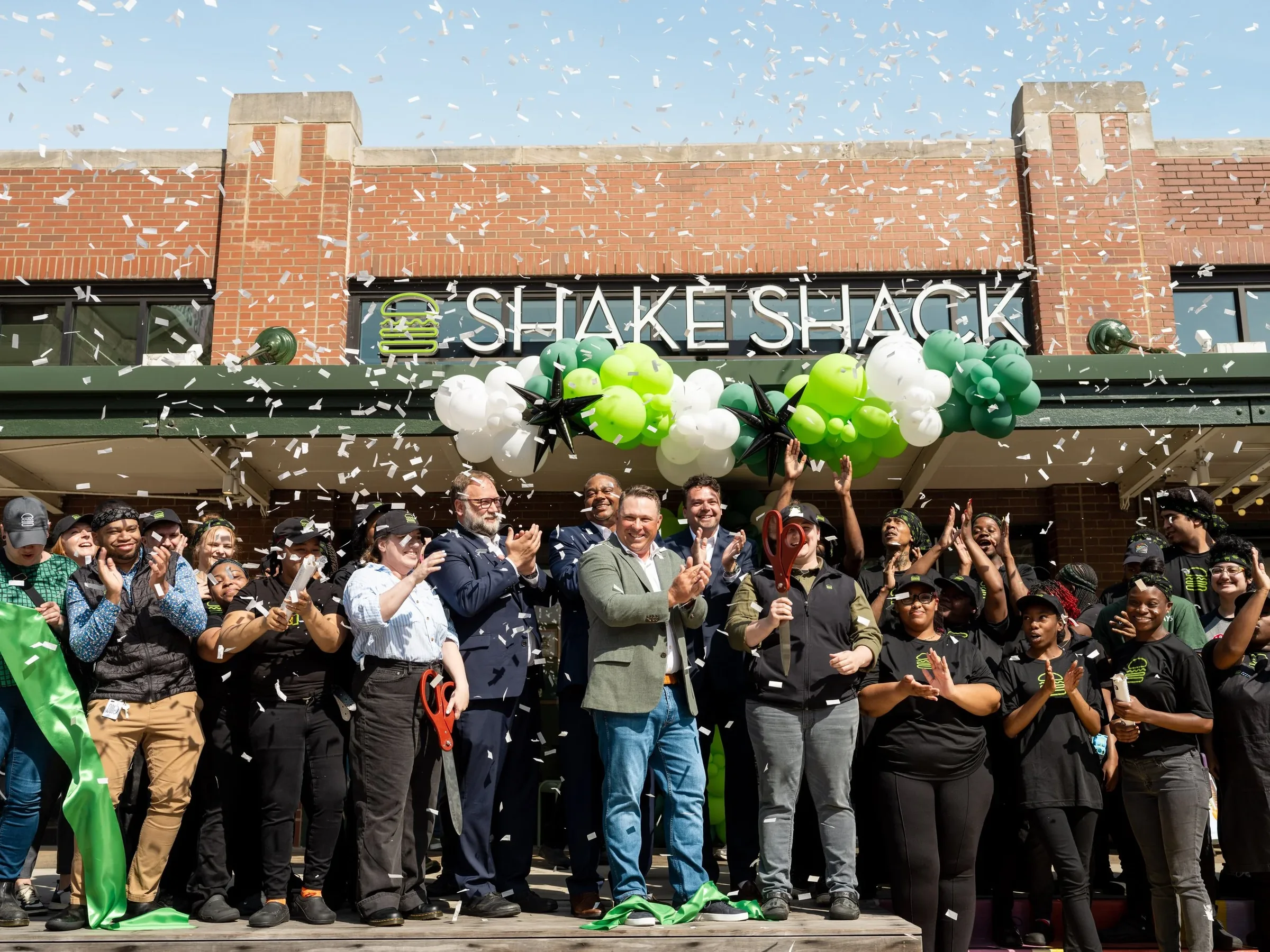 Guests celebrate a Shake Shack ribbon cutting beneath falling confetti.
